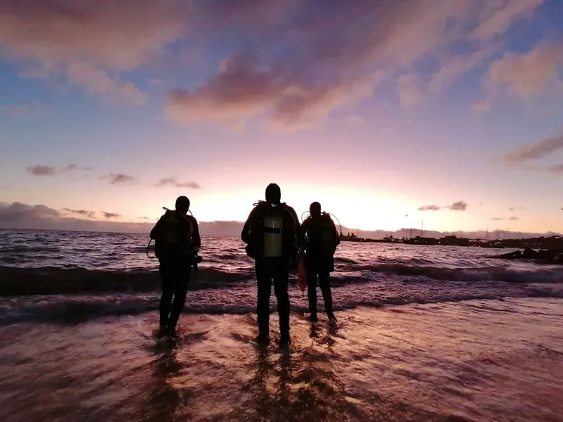 Trois plongeurs équipés se tiennent dans l'eau au coucher du soleil