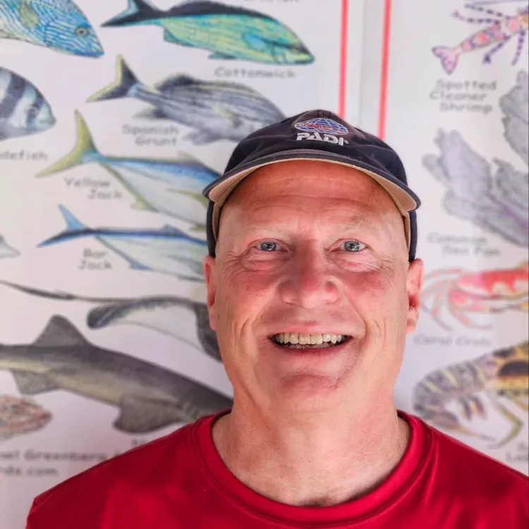 Homme souriant portant une casquette PADI devant un tableau de poissons