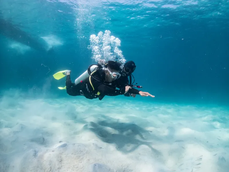 Plongeur en combinaison explore les fonds marins, nageant dans l'eau claire