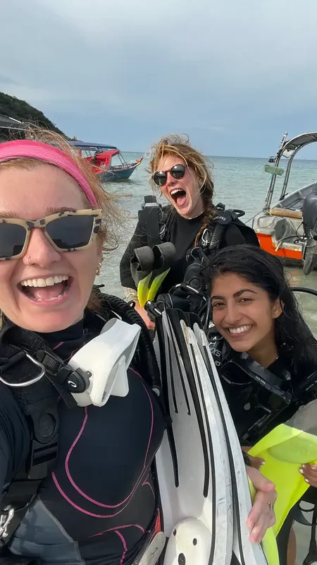 Trois plongeuses souriantes avec leur équipement près de bateaux en mer