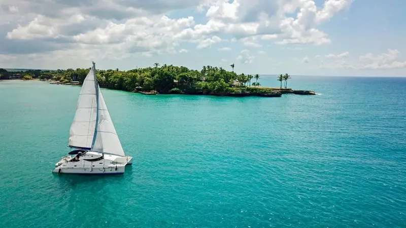 Catamaran à voile naviguant sur une mer turquoise près d'une île