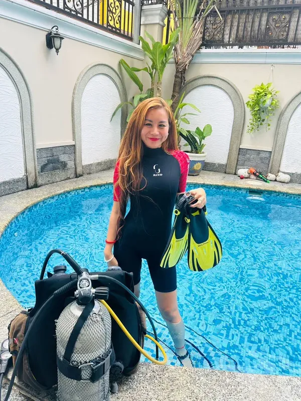 Plongeuse souriante avec combinaison, palmes et bouteille près d'une piscine