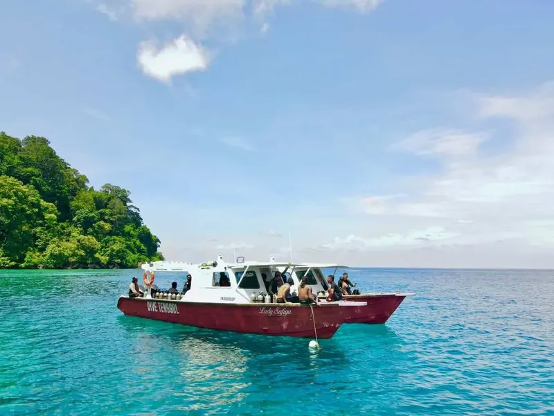 Bateau de plongée rouge avec des passagers en mer turquoise et végétation