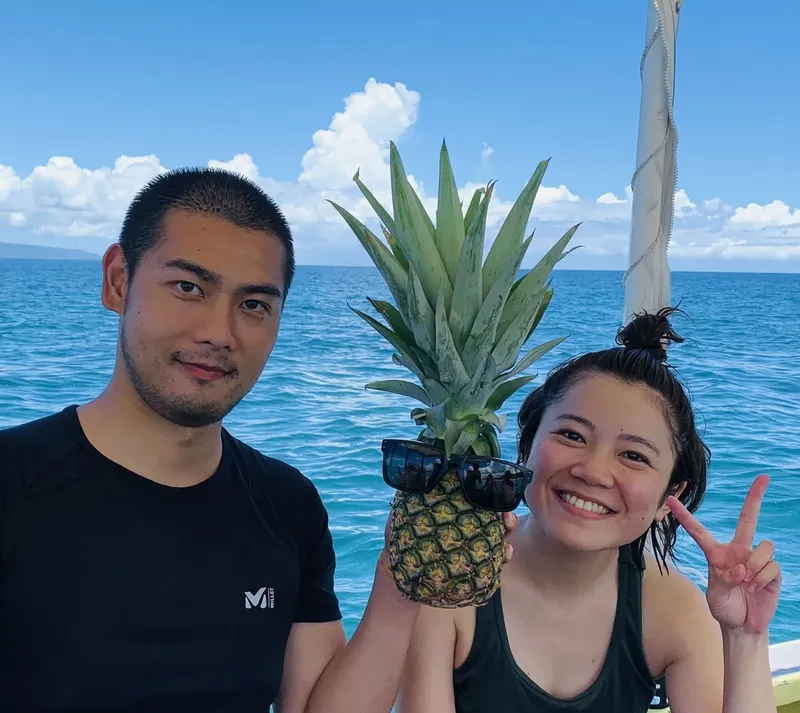 Deux personnes souriantes posent avec un ananas sur un bateau en mer