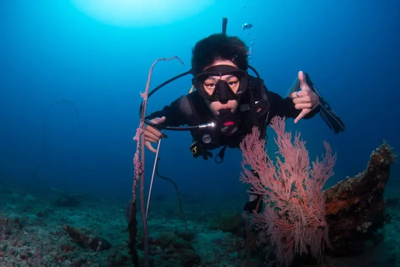 Plongeur souriant avec signe OK, corail et lumière sous-marine