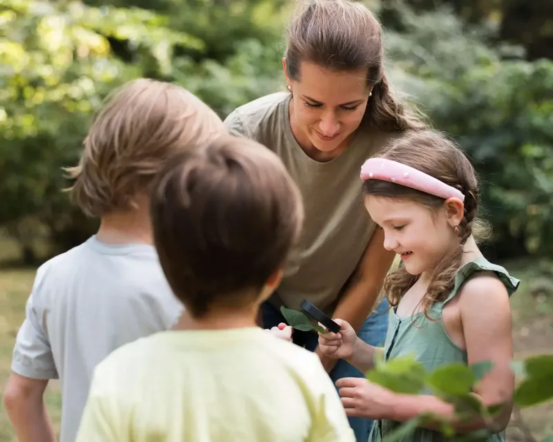 Une adulte et trois enfants observent attentivement une feuille verte