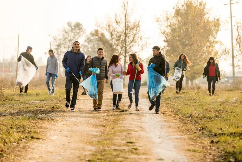 Groupe de personnes marchant sur un chemin rural avec des sacs poubelles