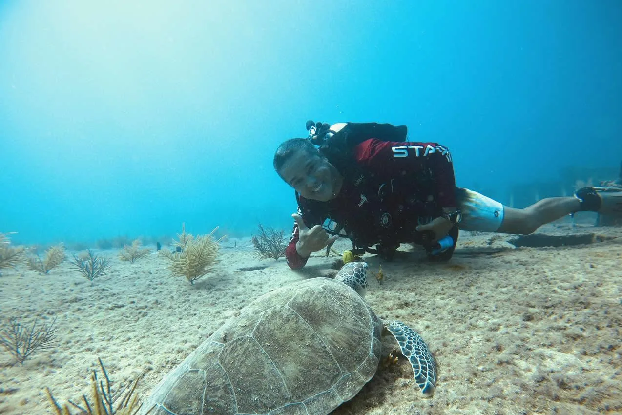 Plongeur souriant interagit avec une tortue marine sur fond sableux