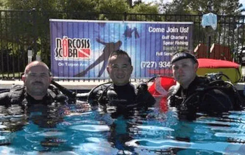 Trois plongeurs souriants dans une piscine devant une grande bannière
