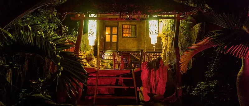 Petite maison éclairée avec végétation luxuriante et ambiance tropicale nocturne