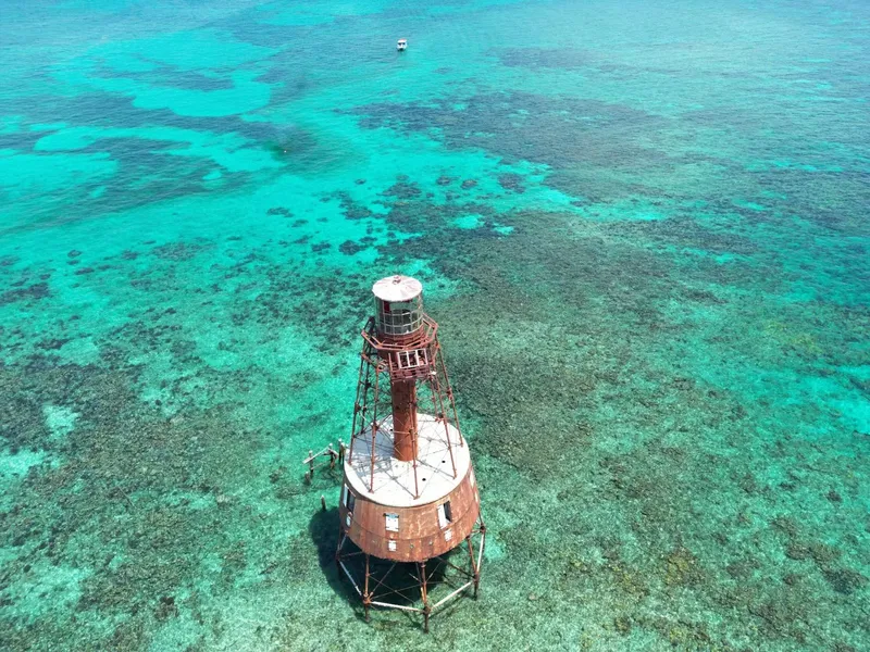 Vue aérienne d'un phare rouillé entouré d'eaux turquoise et de plongeurs