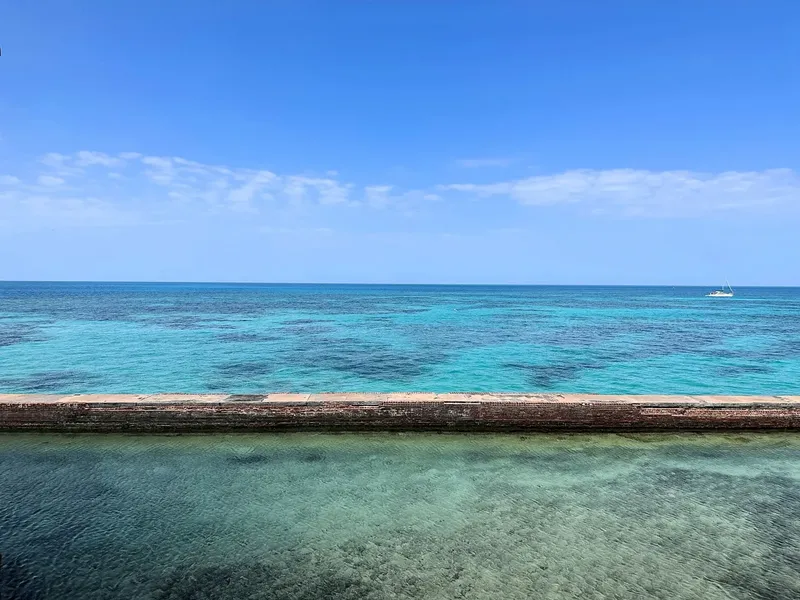 Vue sur mer turquoise avec un bateau à l'horizon et un quai
