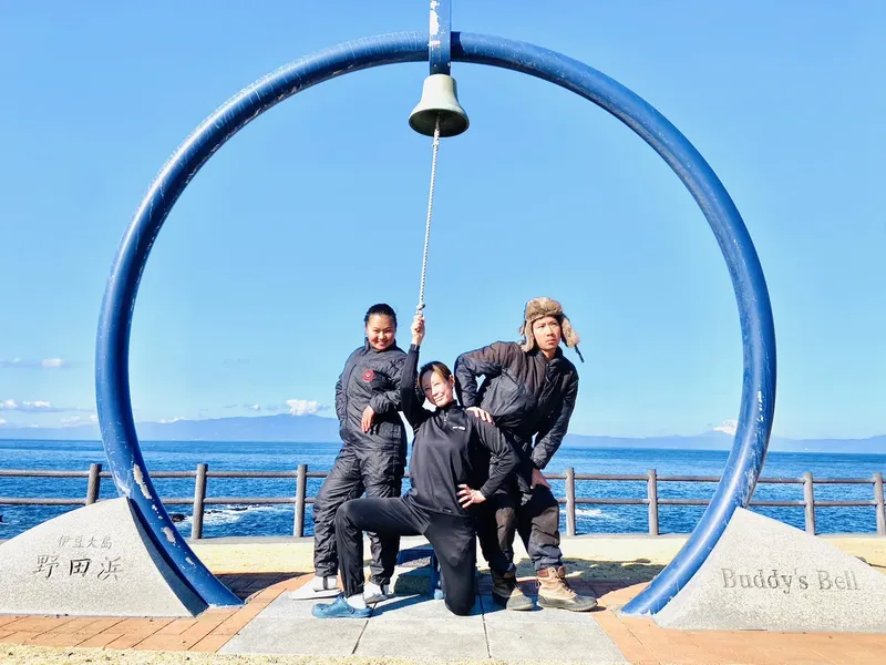 Groupe de plongeurs souriants posant près d'une cloche bleue et de la mer
