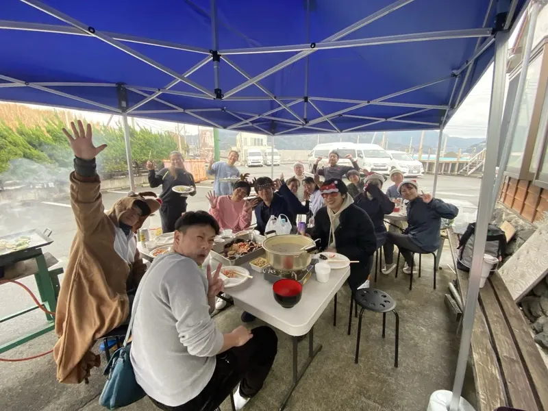 Groupe de personnes mangeant autour d'une table sous un abri bleu
