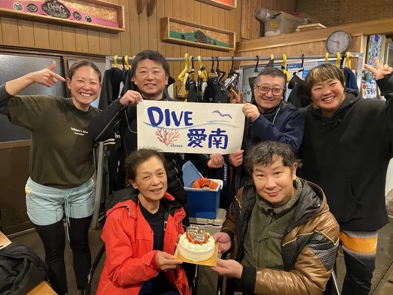 Groupe de personnes souriantes avec un gâteau et une pancarte DIVE