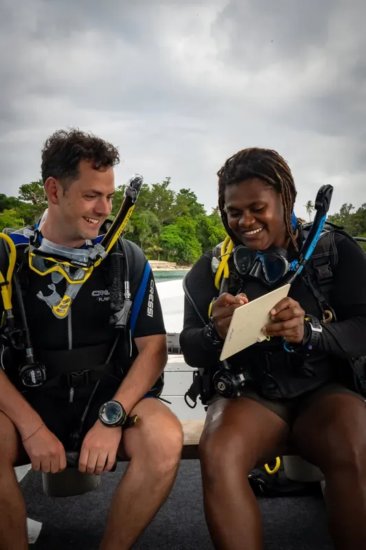 Deux plongeurs souriants équipés discutent sur un bateau en préparation