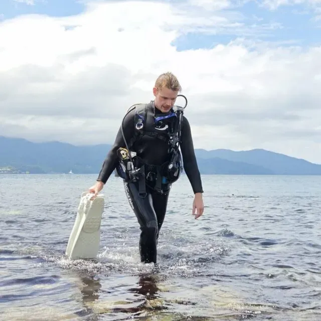 Plongeur en combinaison sortant de l'eau avec une valise blanche