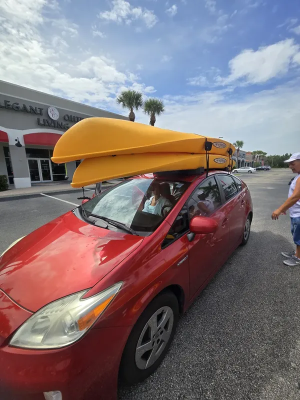 voiture rouge avec deux kayaks jaunes sur le toit dans un parking