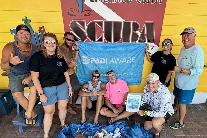 Groupe de plongeurs souriants posant devant une bannière PADI Aware