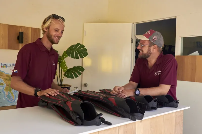 Deux hommes souriants présentent des paires de palmes noires sur un comptoir