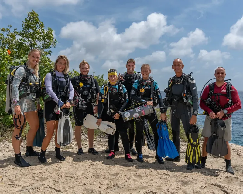 Groupe de plongeurs souriants équipés sur une plage ensoleillée