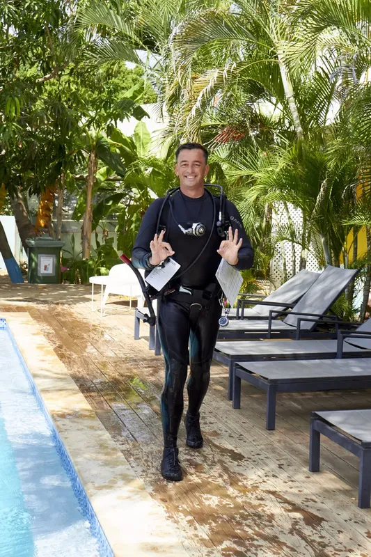 Plongeur en combinaison complète marchant près d'une piscine et de transats