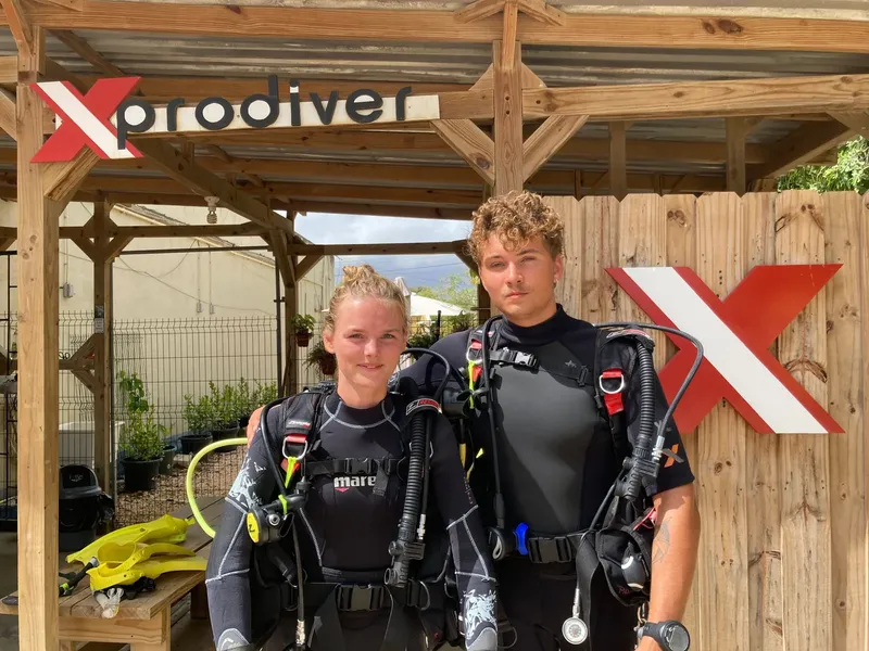 Deux plongeurs souriants équipés devant un centre de plongée ensoleillé