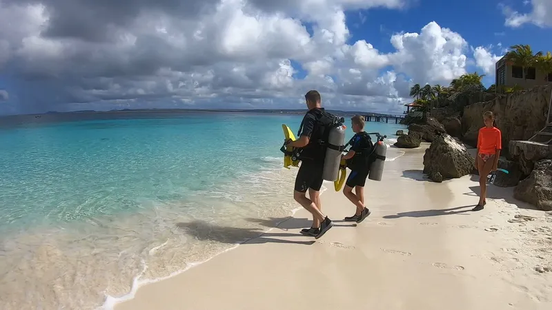 Plage tropicale, deux plongeurs marchant avec leur équipement et une enfant
