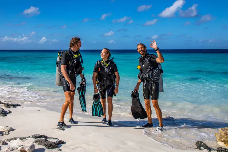 Trois plongeurs souriants sur une plage de sable blanc turquoise