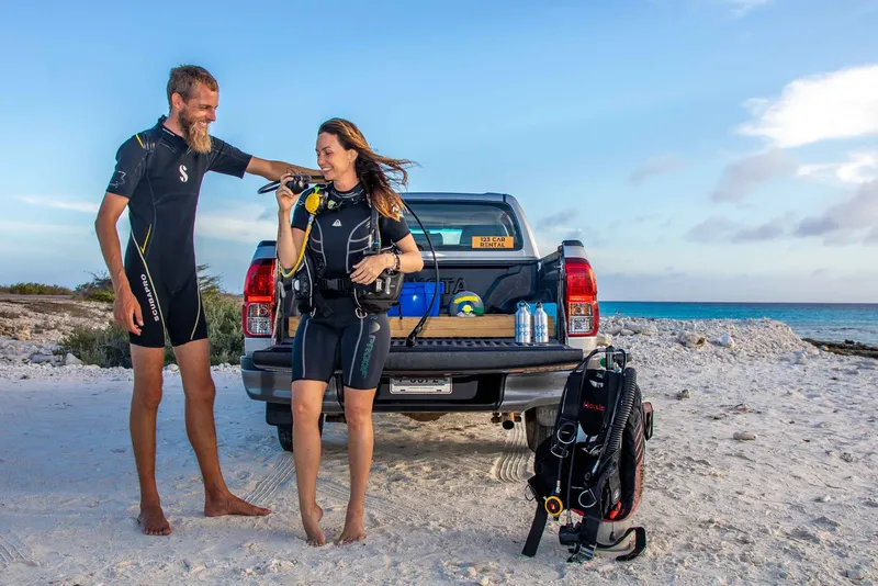 Deux plongeurs équipés près d'un pick-up sur une plage ensoleillée