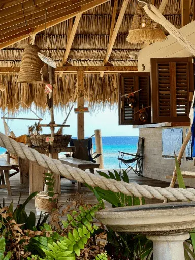 Terrasse ombragée avec vue sur la mer, mobilier en bois et végétation tropicale