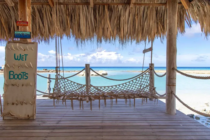 Terrasse en bois avec hamac, vue sur mer turquoise et plage