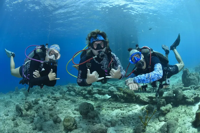 Trois plongeurs souriants font des signes de la main au fond marin