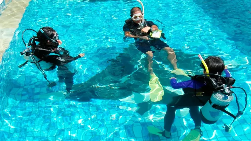 Trois plongeurs s'entrainent dans une piscine, équipement complet visible
