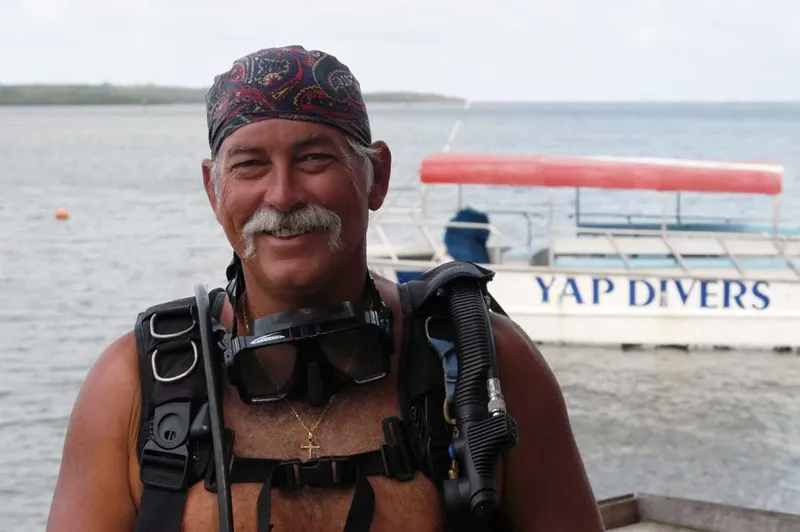 Plongeur souriant avec équipement complet devant un bateau de plongée