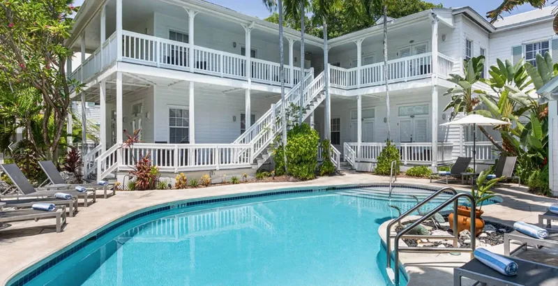 Bâtiment blanc à deux étages avec piscine et chaises longues bleues
