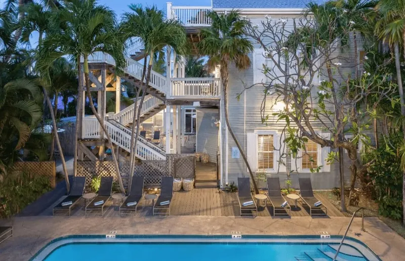 Bâtiment blanc avec escalier, piscine et transats au premier plan
