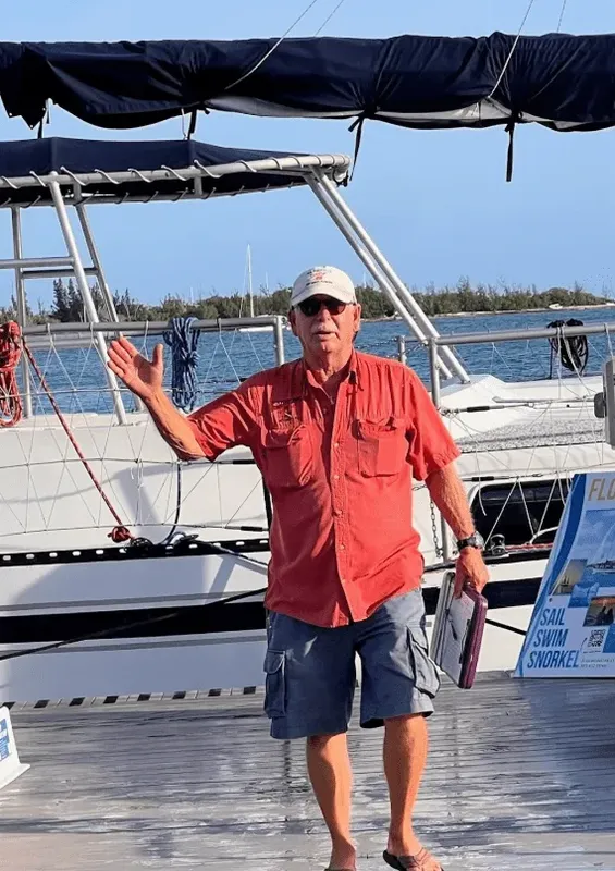 Homme saluant sur un ponton devant un catamaran amarré