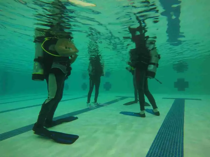 Trois plongeurs en formation dans une piscine, équipement complet visible
