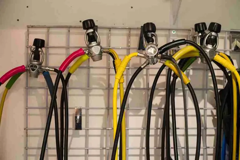 Rangée de détendeurs de plongée colorés accrochés à un mur grillagé