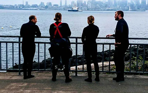 Quatre plongeurs en combinaison regardent la mer et la ville