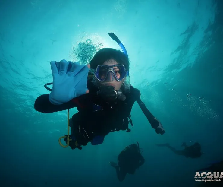 Plongeur souriant avec signe de la main sous l'eau turquoise