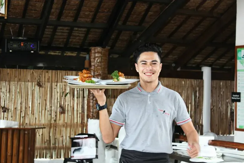 Serveur souriant présentant un plateau de nourriture dans un restaurant extérieur