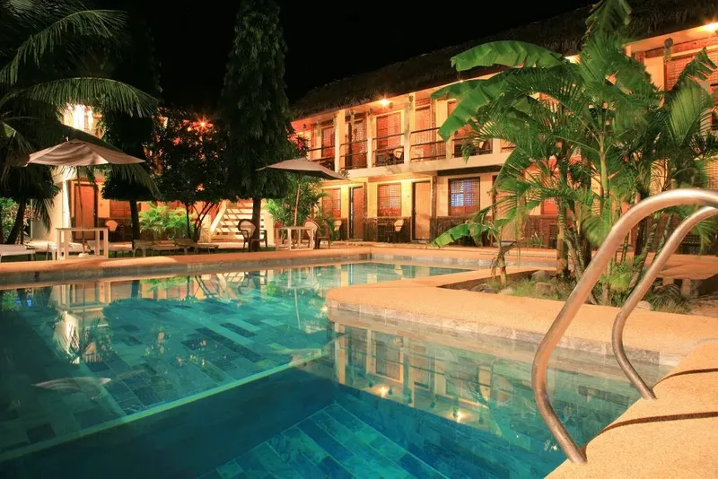 Piscine éclairée devant un bâtiment avec végétation tropicale la nuit