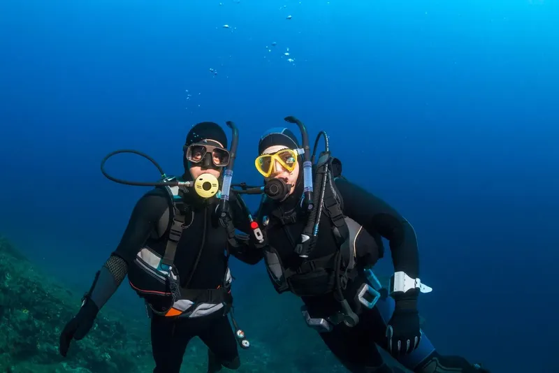 Deux plongeurs souriants en combinaison, masque et détendeur sous l'eau