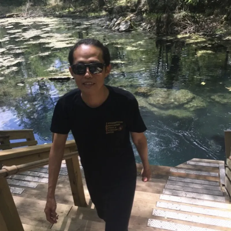 Un homme en t-shirt noir descend des marches en bois près d'une eau claire