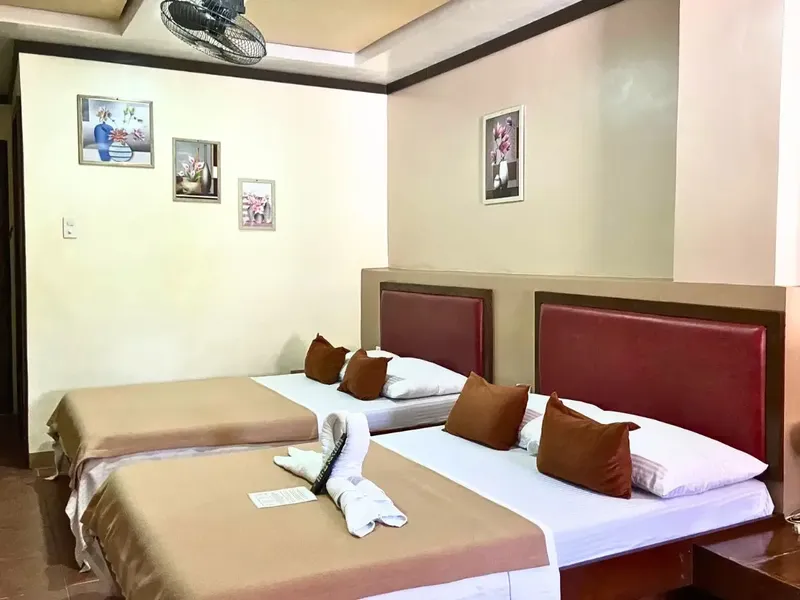 Chambre d'hôtel avec deux lits, décoration sobre et ventilateur au plafond