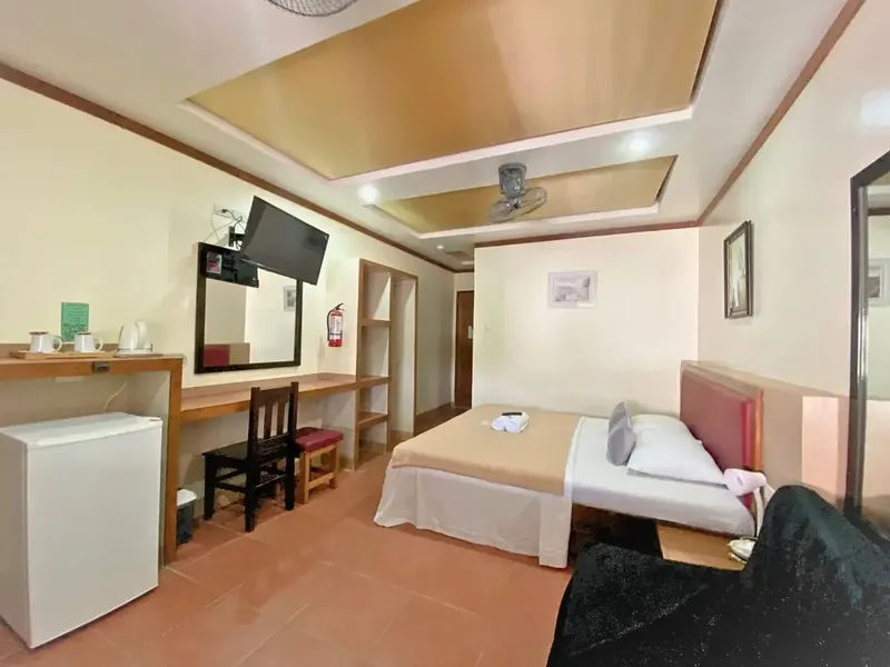 Chambre d'hôtel avec lit, bureau, télévision et petit réfrigérateur blanc