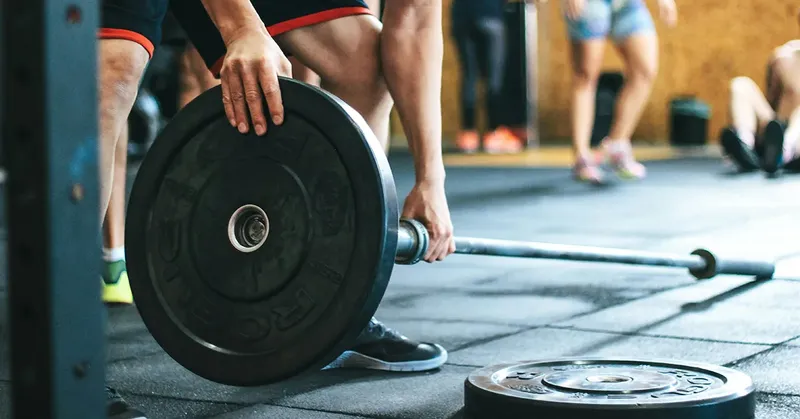 Homme préparant une barre de musculation avec des poids en salle
