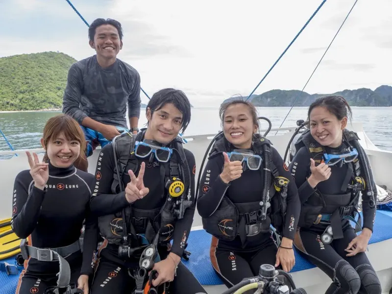 Quatre plongeurs souriants avec leur équipement sur un bateau en mer